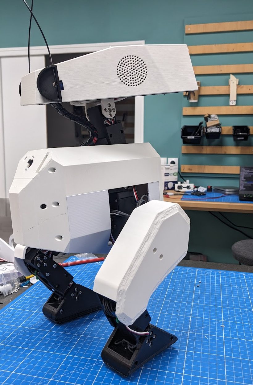 Side view of the Open Duck Mini v2 robot mid-stride, showing the speaker grille on its head and bent servo-driven legs